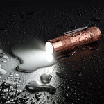 Lumintop FW1AA red copper EDC flashlight IP68 waterproof wet surface water droplets beam on dark background outdoor use